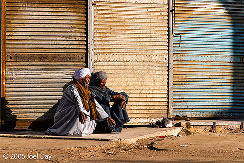 Egyptian men resting in morning light next to closed market stalls, Aswan, Egypt